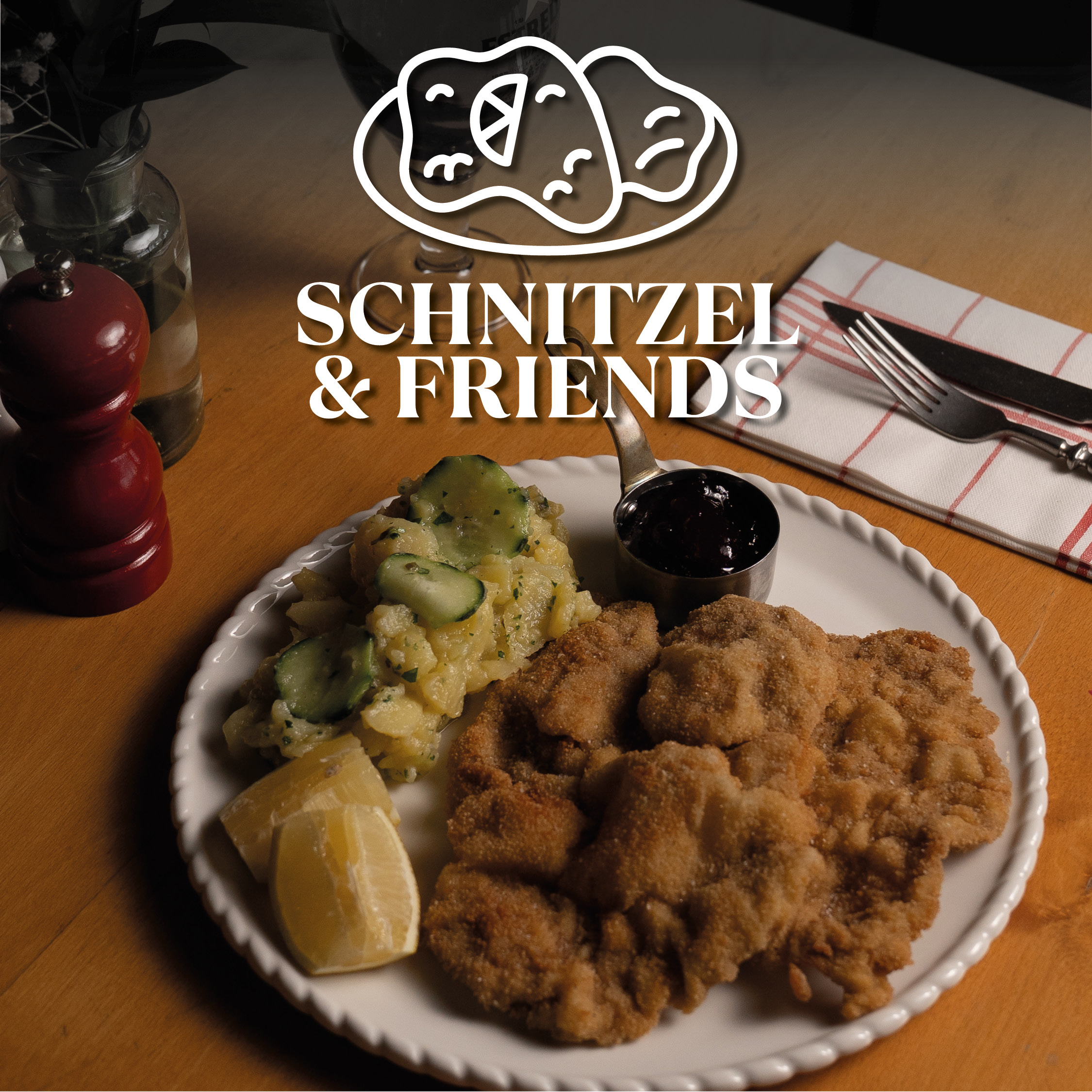 Knuspriges Schnitzel mit Kartoffelsalat und Gurkenscheiben, Zitronenviertel und einer dunklen Sauce in einer kleinen Schale auf einem weißen Teller; oben im Bild ein Logo mit der Aufschrift Schnitzel & Friends.